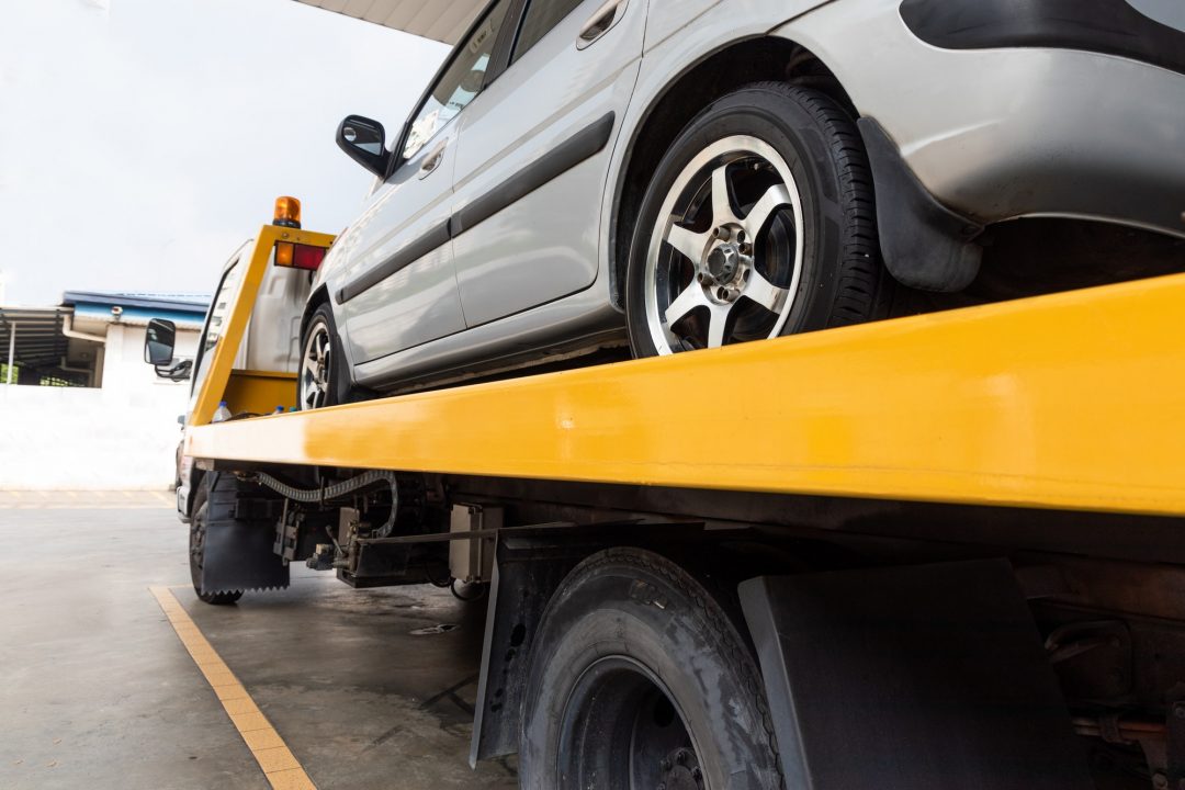 broken car on flatbed tow truck being transported for repair